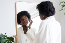 Woman Applying Eye Patch Looking In Mirror