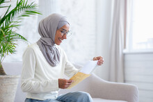 Joyful Woman At Home Received Letter Mail Notification With Good News, Muslim Woman In Hijab Is Happy Sitting On Sofa In Living Room.