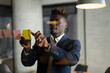 © JustLife - Portrait of successful businessman in office. Young African man witing ideas on colorful stickers on glass wall..