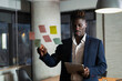 © JustLife - Portrait of successful businessman in office. Young African man witing ideas on colorful stickers on glass wall..