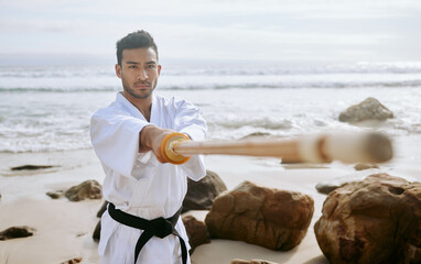 Sticker - A master is a full-time student. Shot of a young martial artist practising karate with a wooden katana on the beach.