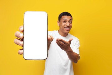 young african american guy in white t-shirt shows blank screen of smartphone on yellow isolated background