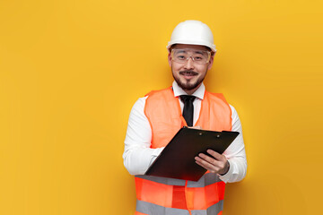 Wall Mural - Asian civil engineer in uniform writes plan on paper and smiles on yellow isolated background