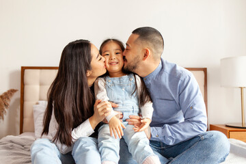 Wall Mural - happy young asian family sit on bed together with daughter, korean little girl hug and love parents at home