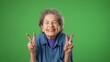 © Robert Peak - Portrait of happy elderly senior old woman with wrinkled skin and grey hair smiling and giving peace or victory sign gesture with hands isolated on green screen background.