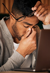Poster - Closeup of young indian man feeling stressed while sitting alone and using a laptop to browse the internet. Mixed race student suffering from a headache while studying late at night. Making mistakes