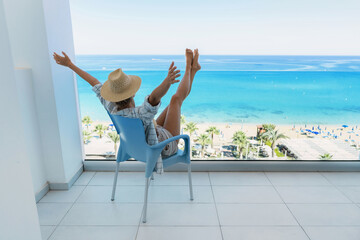 Wall Mural - Young woman relaxing in chair on balcony of beachfront hotel or apartment