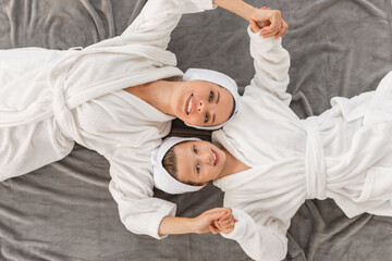 Wall Mural - Happy Mom And Little Daughter In Bathrobes Lying On Bed At Home