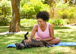 Young multi-ethnic woman gives her dog a tummy tickle on yoga mat in park