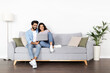 © Prostock-studio - Loving eastern couple sitting on couch at home, using laptop