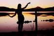 Eine junge Frau tanzt im Sonnenuntergang vor einem See mit Bergen