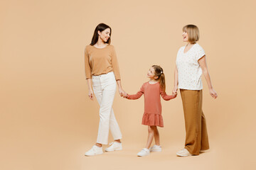 Wall Mural - Full body side view happy fun cool women wear casual clothes with child kid girl 6-7 years old. Granny mother daughter walk holding hands isolated on plain beige background. Family parent day concept.