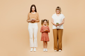 Wall Mural - Full body fun women wearing casual clothes with child kid girl 6-7 years old. Granny mother daughter holding in hand use mobile cell phone isolated on plain beige background Family parent day concept