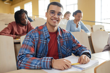 Wall Mural - Portrait of schoolboy in eyeglasses smiling at camera while sitting at desk at lecture