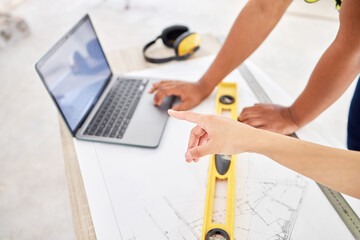 Poster - Lets work with that first. Cropped shot of two unrecognisable contractors standing inside together and using a laptop while planning.