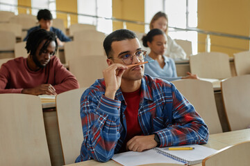 Wall Mural - Scholboy sitting at desk with textbook and listening to teacher while sitting at lecture with his classmates