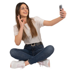 Wall Mural - Woman doing selfie, full length portrait of young caucasian woman doing selfie. Sitting on the floor doing ok sign with hand. Using mobile phone. Transparent png image. Lifestyle concept idea.