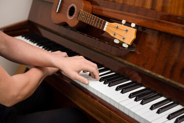 Wall Mural - A young guy plays a complex piece of music on the piano, his hands lie on the keys in a cross, the guy loves music very much and often plays both the piano and ukulele