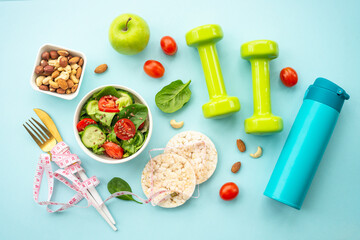 Diet food, healthy lifestyle and fitness background. Vegan salad, crispbread, fruits and dumbells on blue. Flat lay.