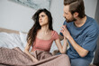 Brunette man touching hand of upset and asexual girlfriend on bed at home.