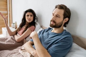 Wall Mural - Indifferent man looking away while angry girlfriend quarrelling in bedroom.