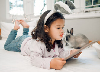 Wall Mural - Perfect way to keep them busy. Shot of an adorable little girl lying on her bed with a digital tablet.