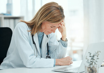 Poster - I have such a bad headache. Shot of a mature doctor sitting alone in her clinic and feeling stressed while using her laptop.
