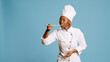 African american cook doing food taste test with spoon, sipping soup for taste testing on camera. Young gourmet chef in apron tasting restaurant meal over blue background, tasty food.