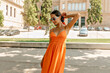 © PhotoBook - slim tender girl with dark hair wearing bright summer dress and bright glasses is looking down and smiling outdoor in city park. Cheerful young caucasian girl smiling in camera spends time outdoor.