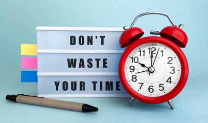Poster - text don't waste your time written on the lightbox with alarm clock and colorfull stickers on blue b