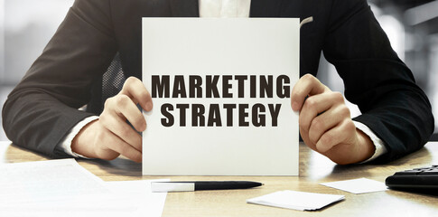 Poster - Businessman holding a white card with text MARKETING STRATEGY on office background