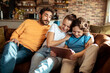 © Baba Images - Young family using a tablet on the couch in the living room of their home