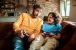 © Baba Images - Father and son playing videos games on a gaming console in the living room of their home