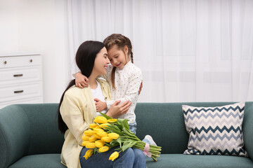 Sticker - Happy woman with her daughter and bouquet of yellow tulips on sofa at home, space for text. Mother's day celebration