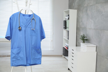 Sticker - Blue medical uniform and stethoscope hanging on rack in clinic. Space for text