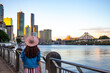 beautiful long hair woman in a hat watching the sunset over brisbane city; city reach boardwalk with amazing view of large skyscrapers by brisbane river, australia, holidays in brisbane