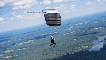 Skydiver flying parachute canopy over lake and fields with clouds