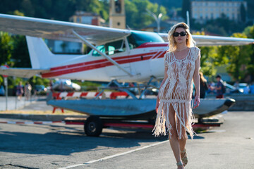 Summer vacation on Como lake Italy. Elegant woman in trendy dress walking in street of European city. Sexy woman posing on the street near jet plane.