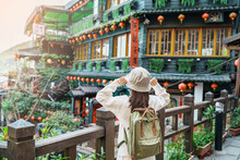 Woman Traveler Visiting In Taiwan, Tourist With Hat And Backpack Sightseeing In Jiufen Old Street Village With Tea House Background. Landmark And Popular Attractions Near Taipei City. Travel Concept