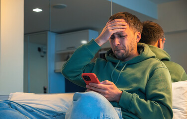 Wall Mural - Man in trouble emotionally reacts to bad news that he read on phone or had fight over the call. Depressed guy at home with smartphone on bed.