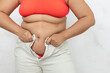 © Юля Бурмистрова - Cropped adipose woman in orange lingerie try to fasten white trousers in studio. Diet, healthy lifestyle, weight loss dieting. Overweight and excess fat problem, fight against visceral fat. Copy space