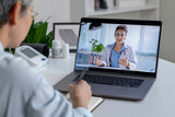 Fototapeta Łazienka - Asian woman with laptop during an online consultation with her doctor in her living room, telemedicine concept