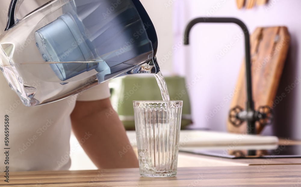 Man pouring water from filter jug into glass on kitchen counter, closeup
