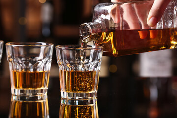 Woman pouring tasty rum from bottle into glasses at table in bar