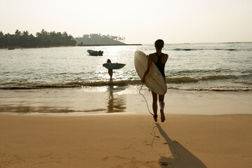 African american woman running with surfboard on ocean beach. Black female surfer with surf board. Pretty multiethnic girl goes on surfing session on tropical location spot at sunny sunrise.