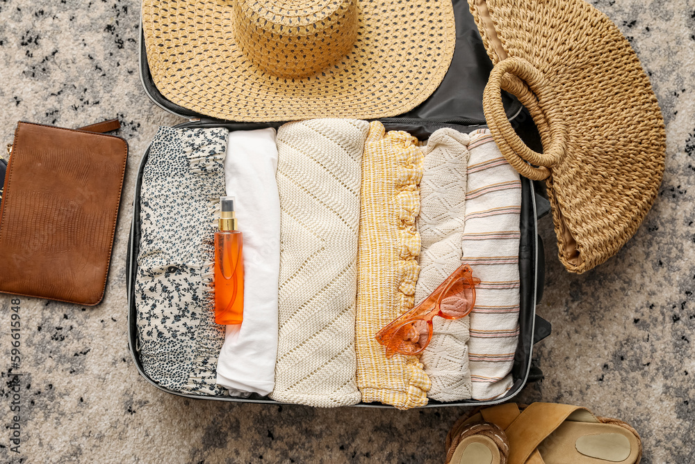 Suitcase with summer clothes and accessories on color carpet