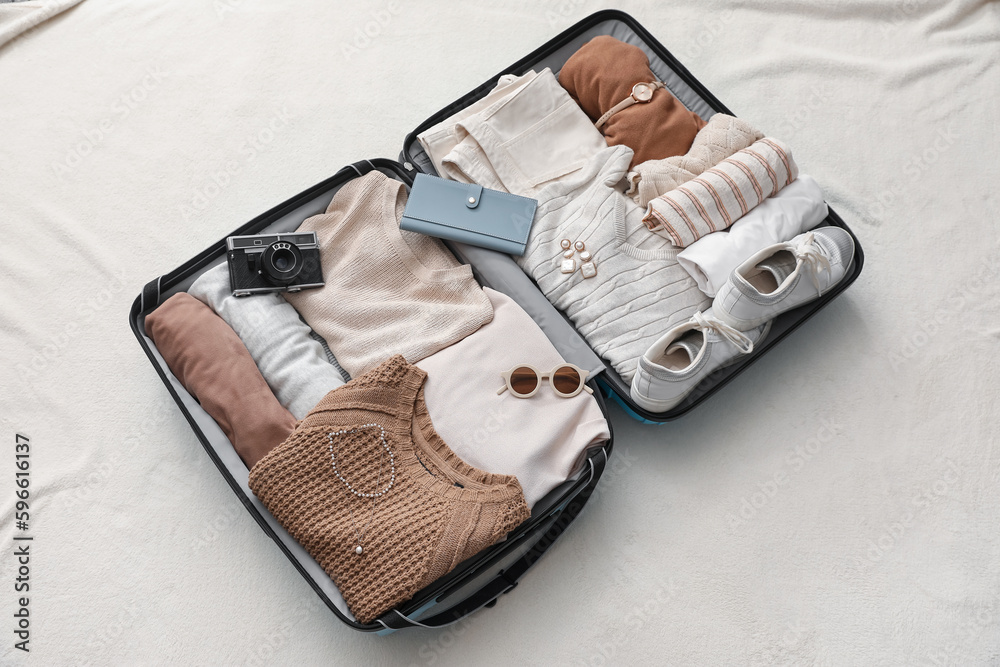 Suitcase with female clothes and accessories on white blanket