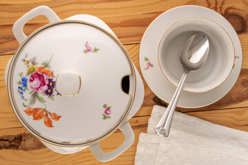 Wall Mural - One old porcelain tureen, soup plate and metal spoon on wooden table, macro, top view.