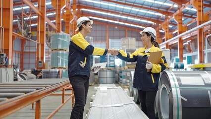 Wall Mural - Two manufacturing employees standing and shaking hands while working at factory manufacturing success teamwork collaboration