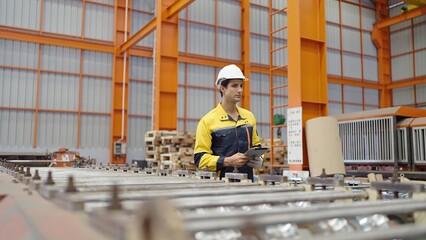 Wall Mural - Young industry worker hispanic latina man in uniform and helmet holding tablet walking and checking stock of steel metal at industry manufacturing factory